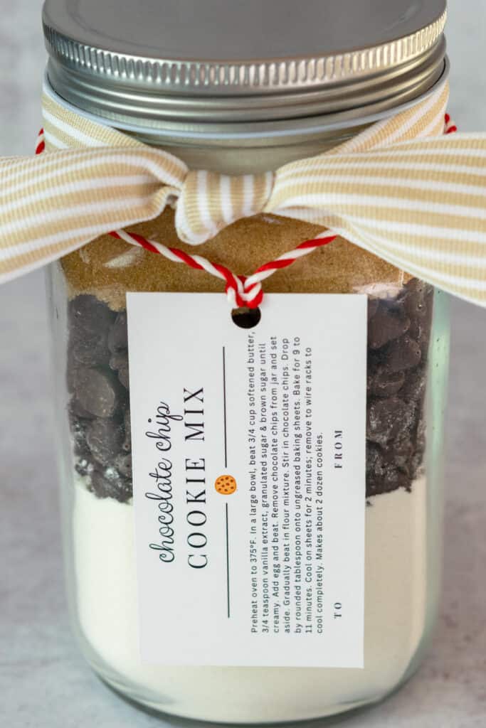 Chocolate chip cookie mix neatly layered in a mason jar with a printable label hanging on the jar.