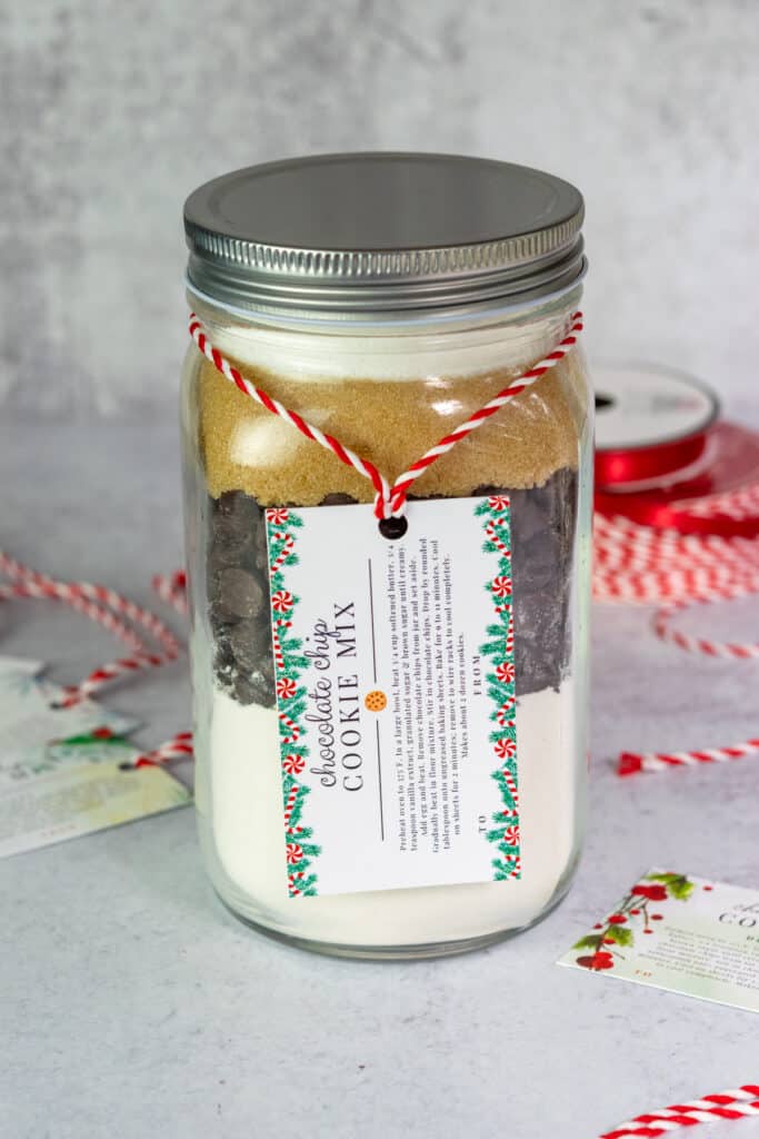 Layered chocolate chip cookie mix in a jar with a Christmas gift tag that has the cookie baking instructions on it.
