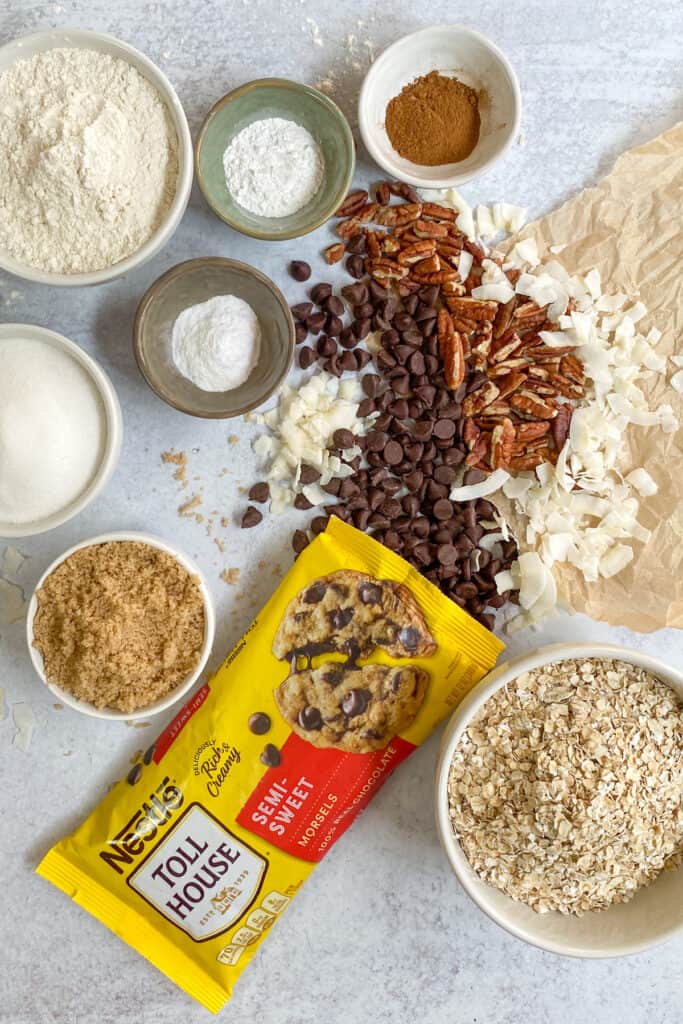 All the ingredients for this cowboy cookie recipe, including chocolate chips, pecans, coconut flakes, rolled oats, granulated sugar, brown sugar, flour, cinnamon, and baking soda and baking powder.