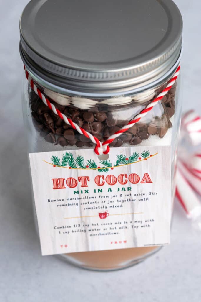 A quart size jar filled with layered hot cocoa mix with a gift tag.