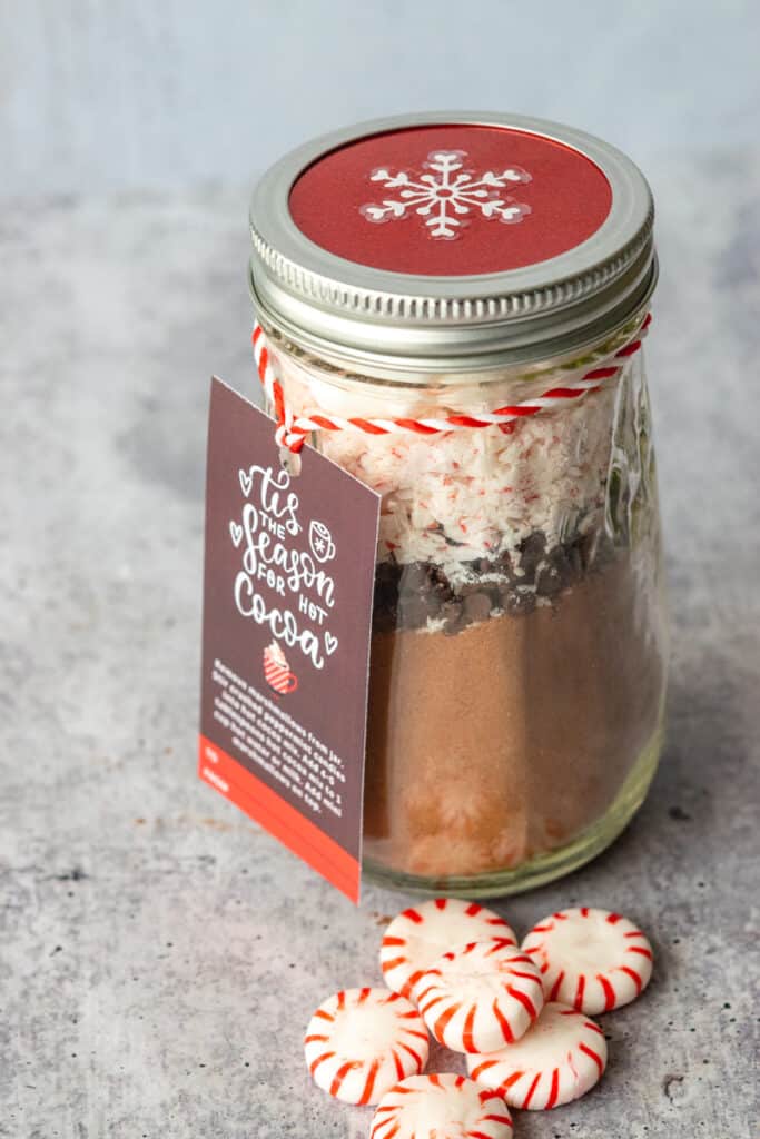 Homemade peppermint hot chocolate mix in a jar with a gift tag and hot cocoa instructions tied on with peppermint-striped string.