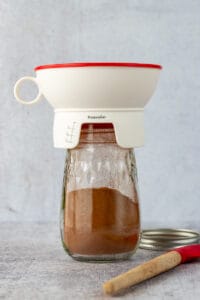 Hot chocolate powder mix in bottom of a mason jar that has a canning funnel on it.