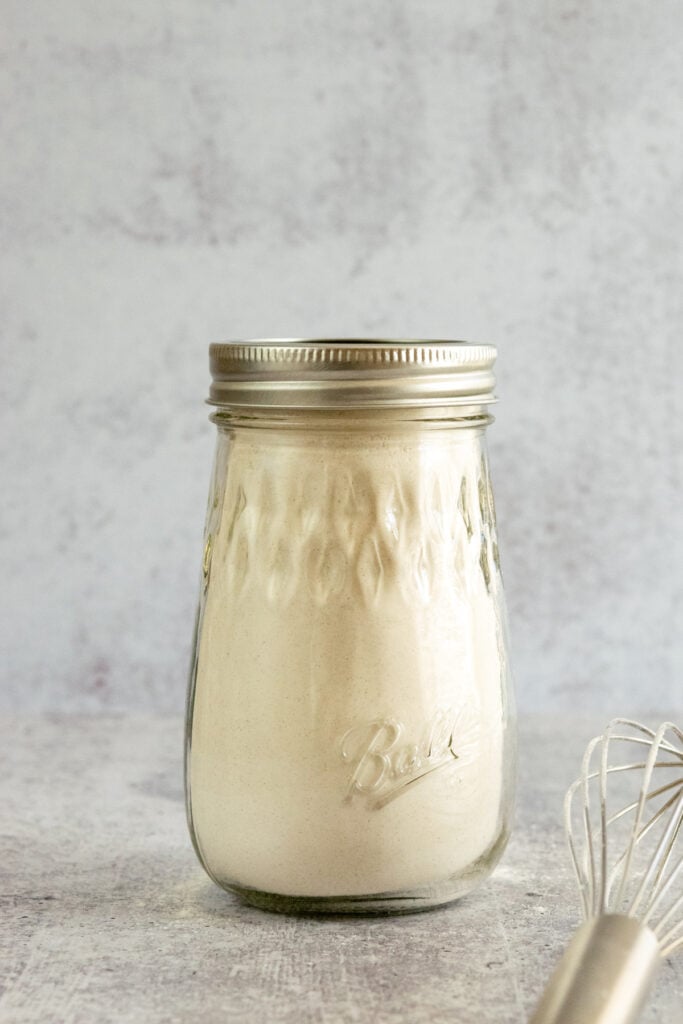 Jar of homemade pancake mix with flour-covered whisk next to it.