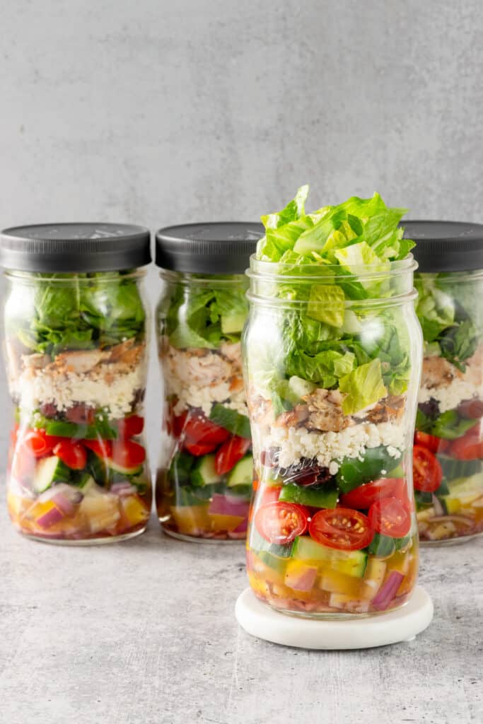 Four quart size mason jars of Greek Salad lined up.