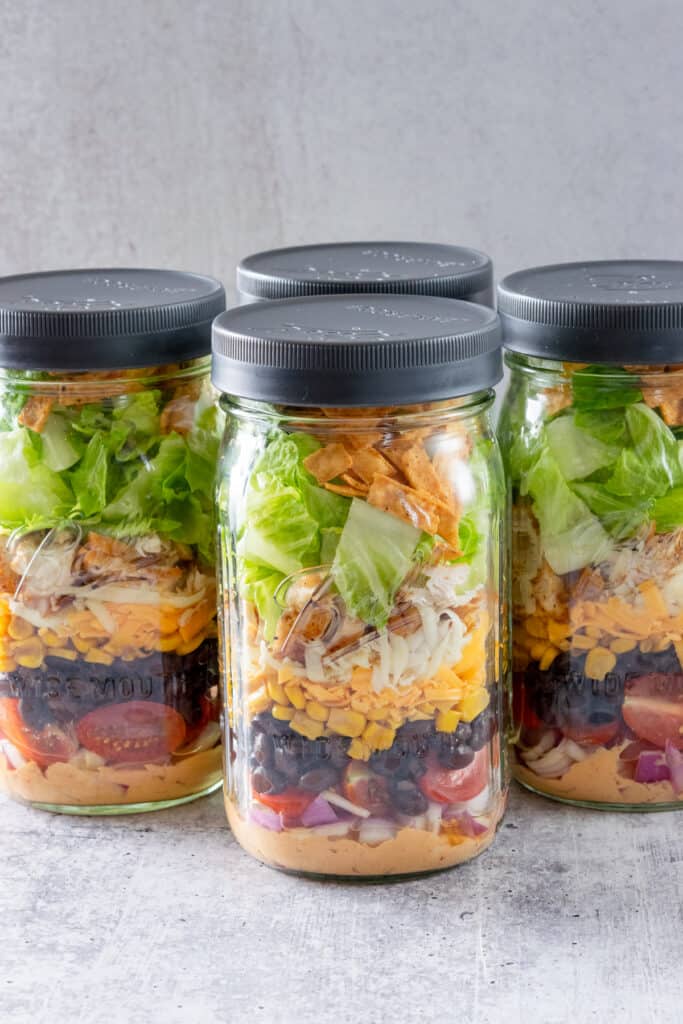 Four mason jars layered with Southwest Chicken Salad and dressing.