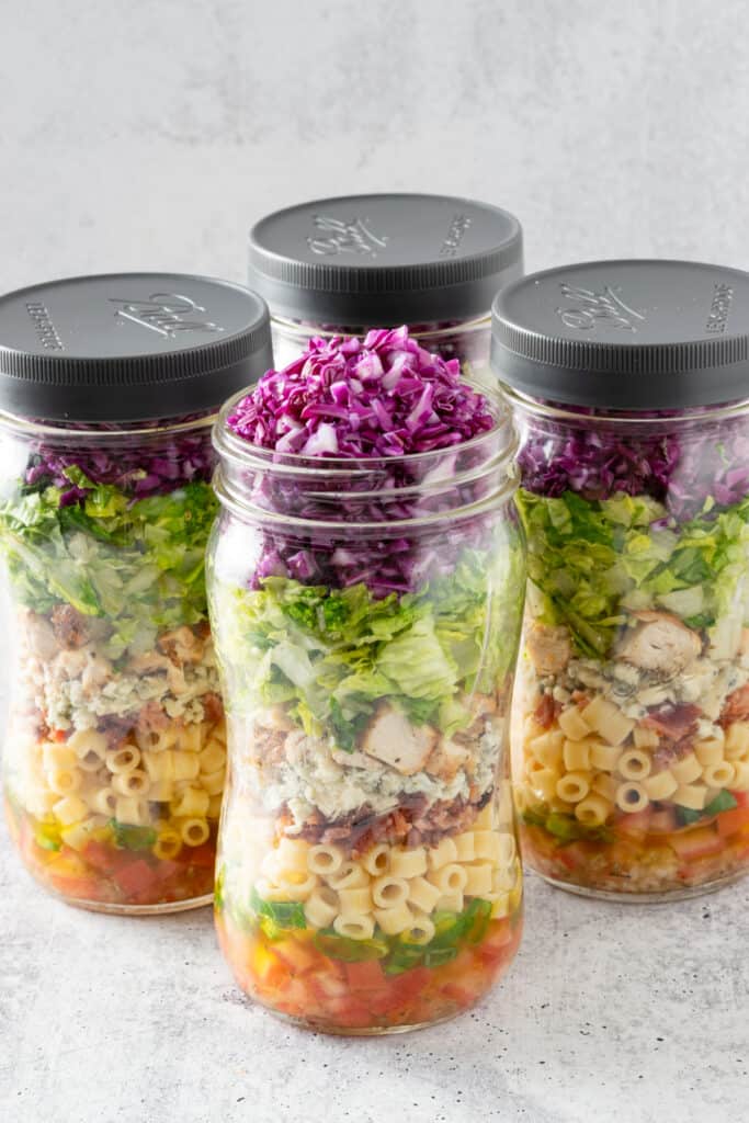 Four chopped salads in a jar, three with lid screwed on and one with no lid and cabbage coming out.