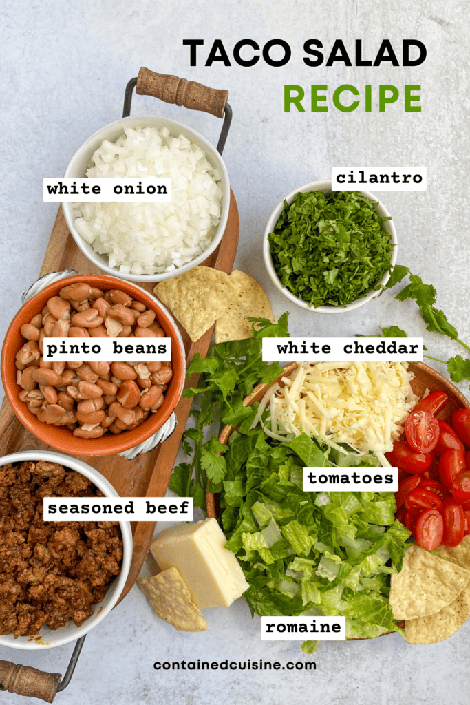 Overhead picture of all the ingredients needed to make taco salad in small bowls, including diced white onion, pinot beans, seasoned beef, shredded cheddar cheese, chopped lettuce, halved cherry tomatoes and chopped cilantro.