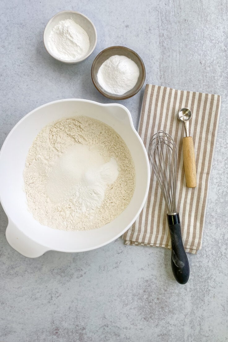 Dry pancake mix ingredients in a white mixing bowl next to a whisk and teaspoon.