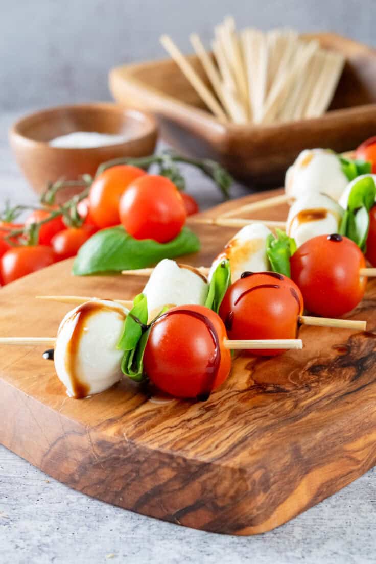 Close up picture of a Caprese skewer kabob showing the mini mozzarella ball, folded basil leaf and cherry tomato skewered onto a stick with drizzle of olive oil and balsamic on top.