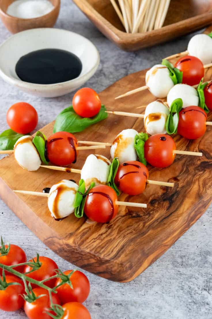 Wooden board with caprese salad skewers drizzled in olive oil and balsamic glaze for a party appetizer.