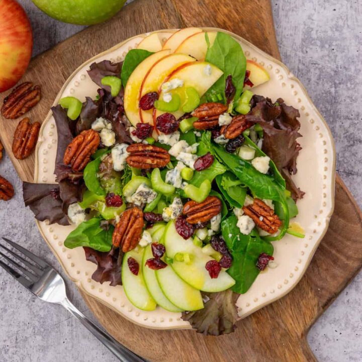 A fall salad loaded with apples, pecans, cranberries and blue cheese, next to a granny smith apple and a honeycrisp apple.