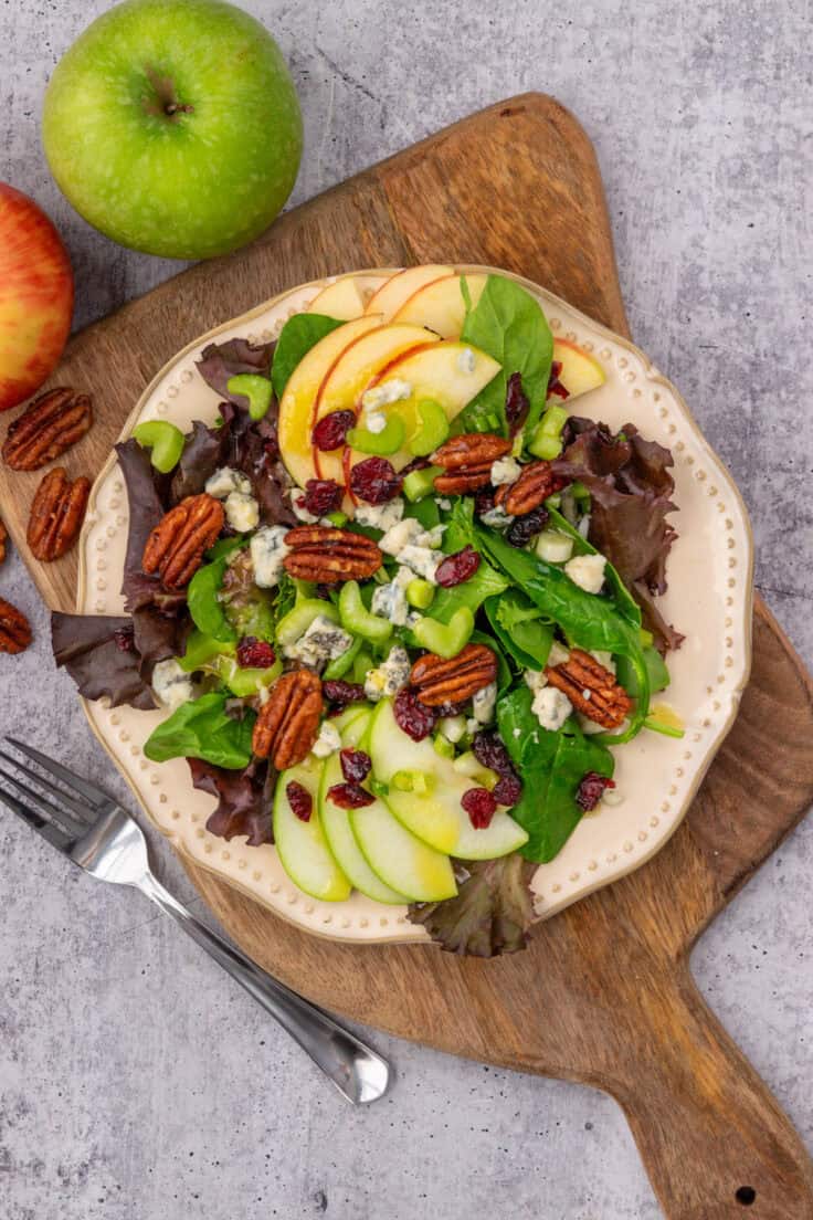 A fall salad loaded with apples, pecans, cranberries and blue cheese, next to a granny smith apple and a honeycrisp apple.