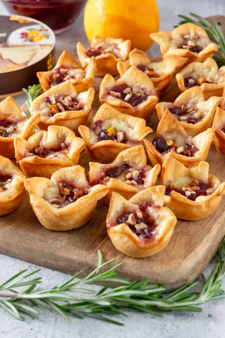 An appetizer of cranberry brie bites on a serving board that's garnished with sprigs of rosemary.