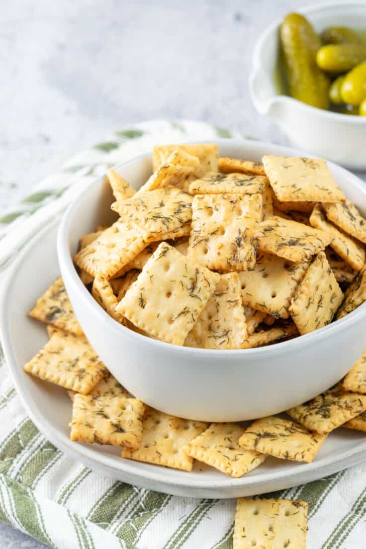 Mini dill pickle saltine crackers in a bowl to snack on which is sitting in front of a small bowl of mini dill pickles.