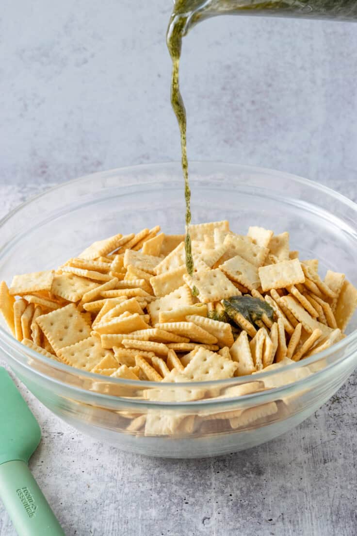 The dill seasoned melted butter being poured onto a bowl full of mini saltine crackers.