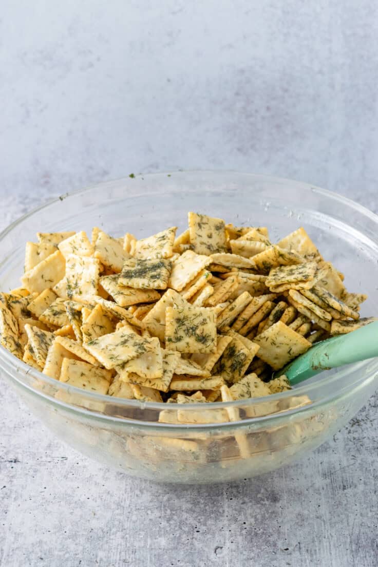 Stirring the dill seasoned butter all over the saltines with a green rubber spatula so all the crackers are coated.