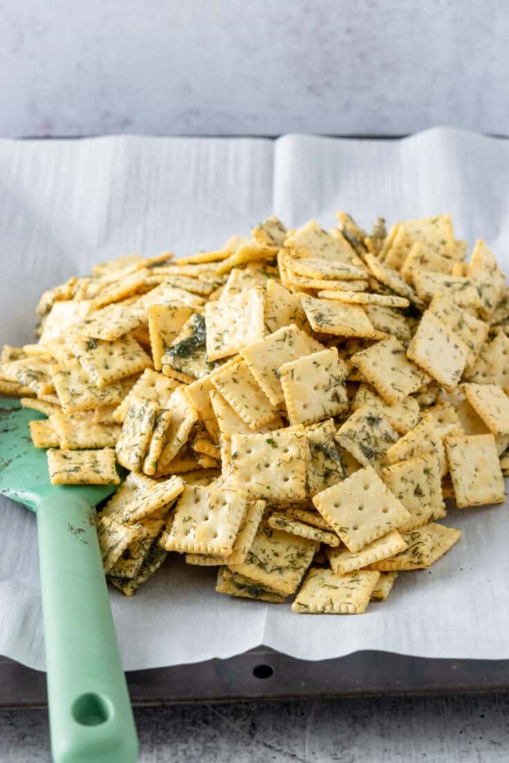 Spreading the buttery dill saltine crackers onto a baking tray that's lined with parchment paper.