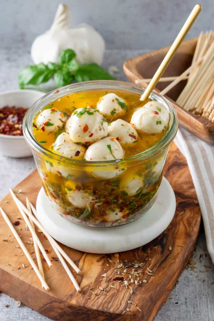 Bowl of marinated mozzarella balls being served as an appetizer on a wooden platter with some party picks to the side.