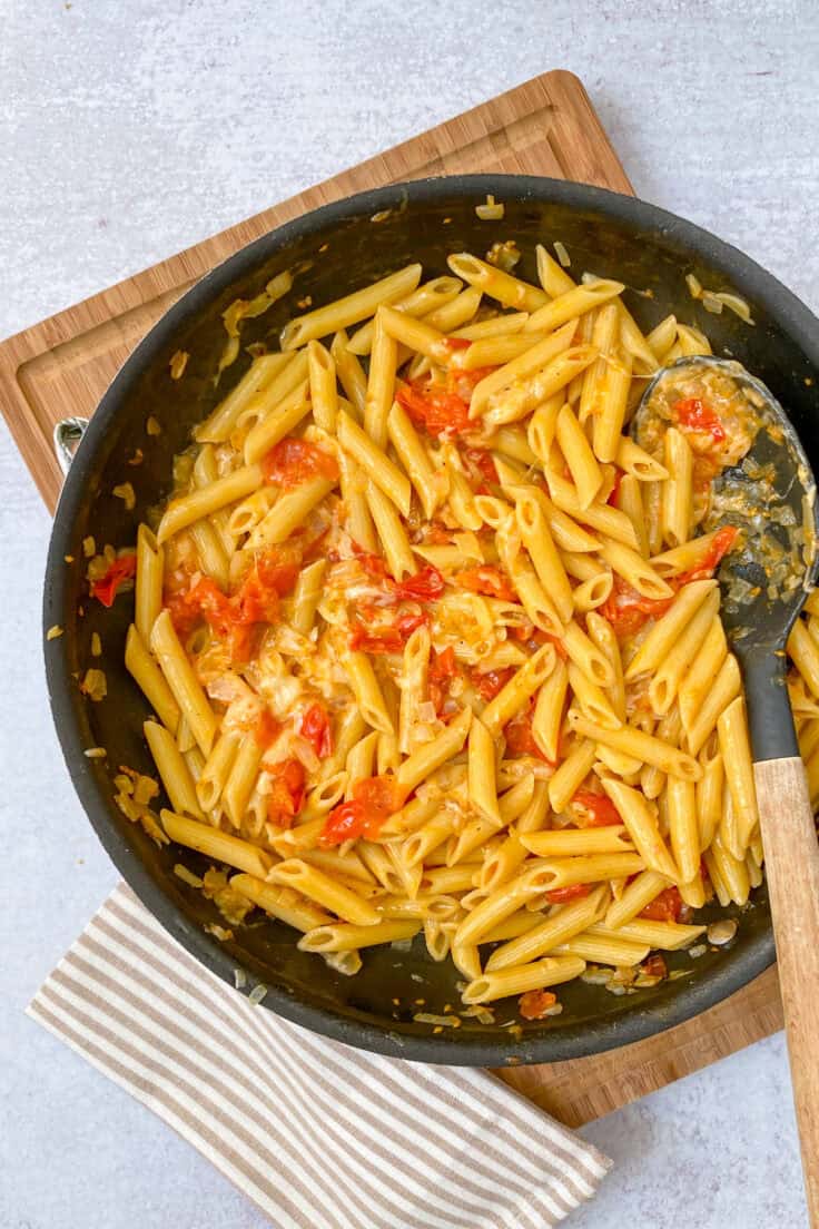 Cooked penne pasta and parmesan added to skillet with cherry tomato sauce.