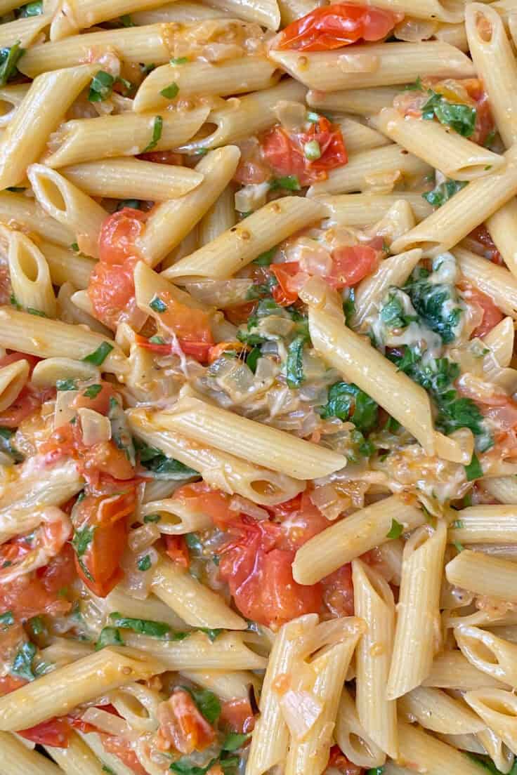 Close up picture showing cooked pasta smothered in cherry tomatoes, basil, parsley and melted parmesan cheese.