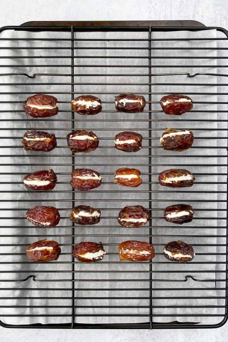 Stuffed dates lined up on a rack which is resting on top of a parchment paper lined baking tray.