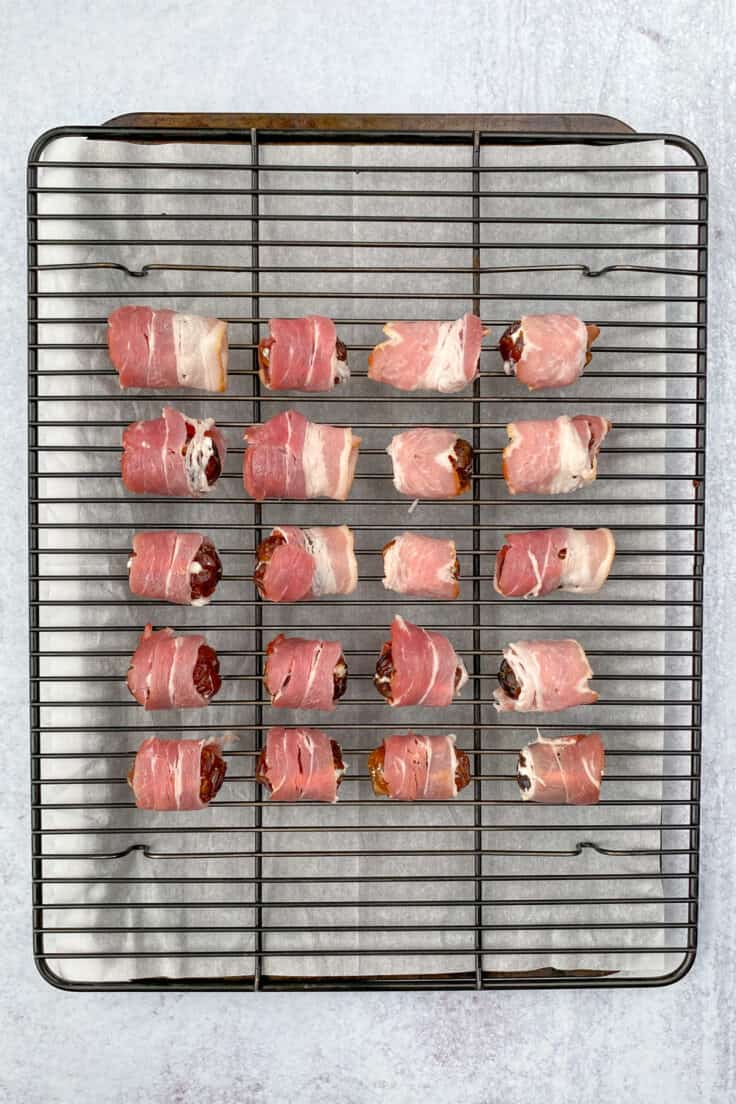 Stuffed dates wrapped with half strips of bacon on a tray before being baked.