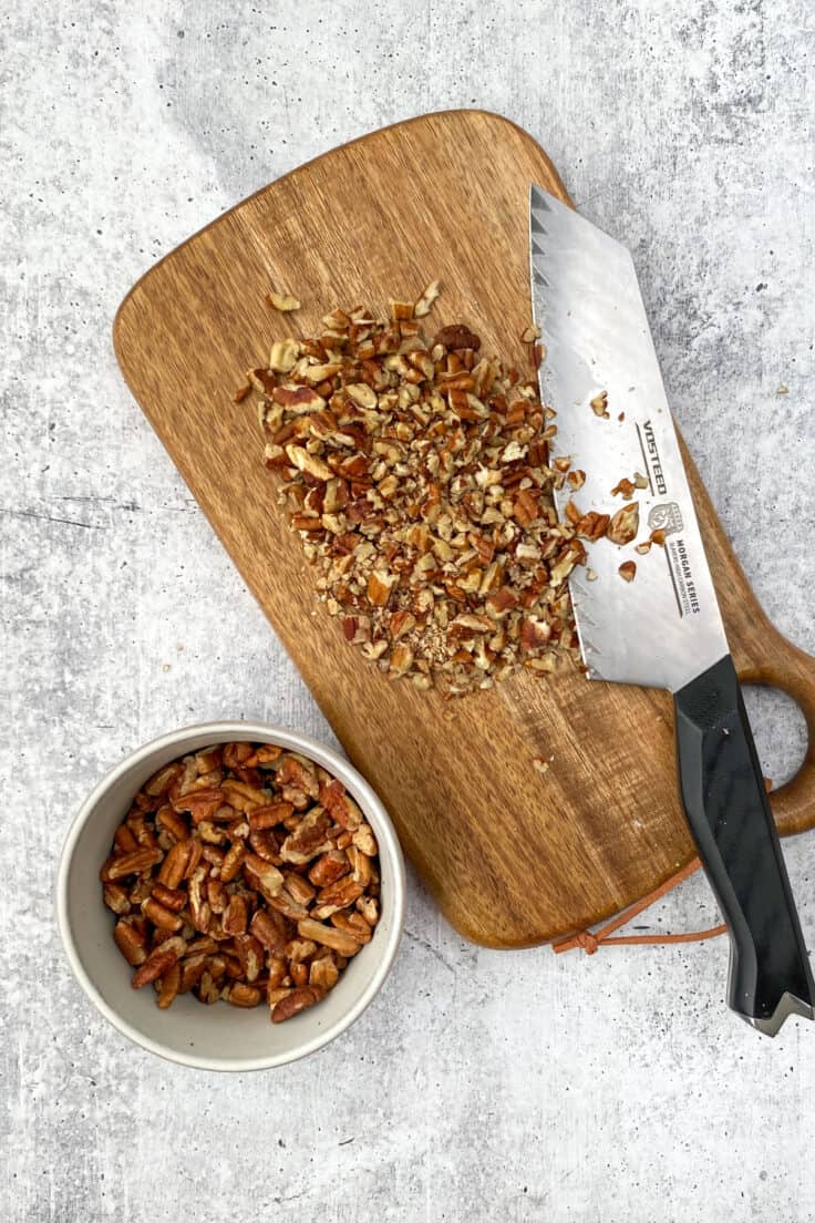 Chopped pecans on a wooden cutting board with a knife.