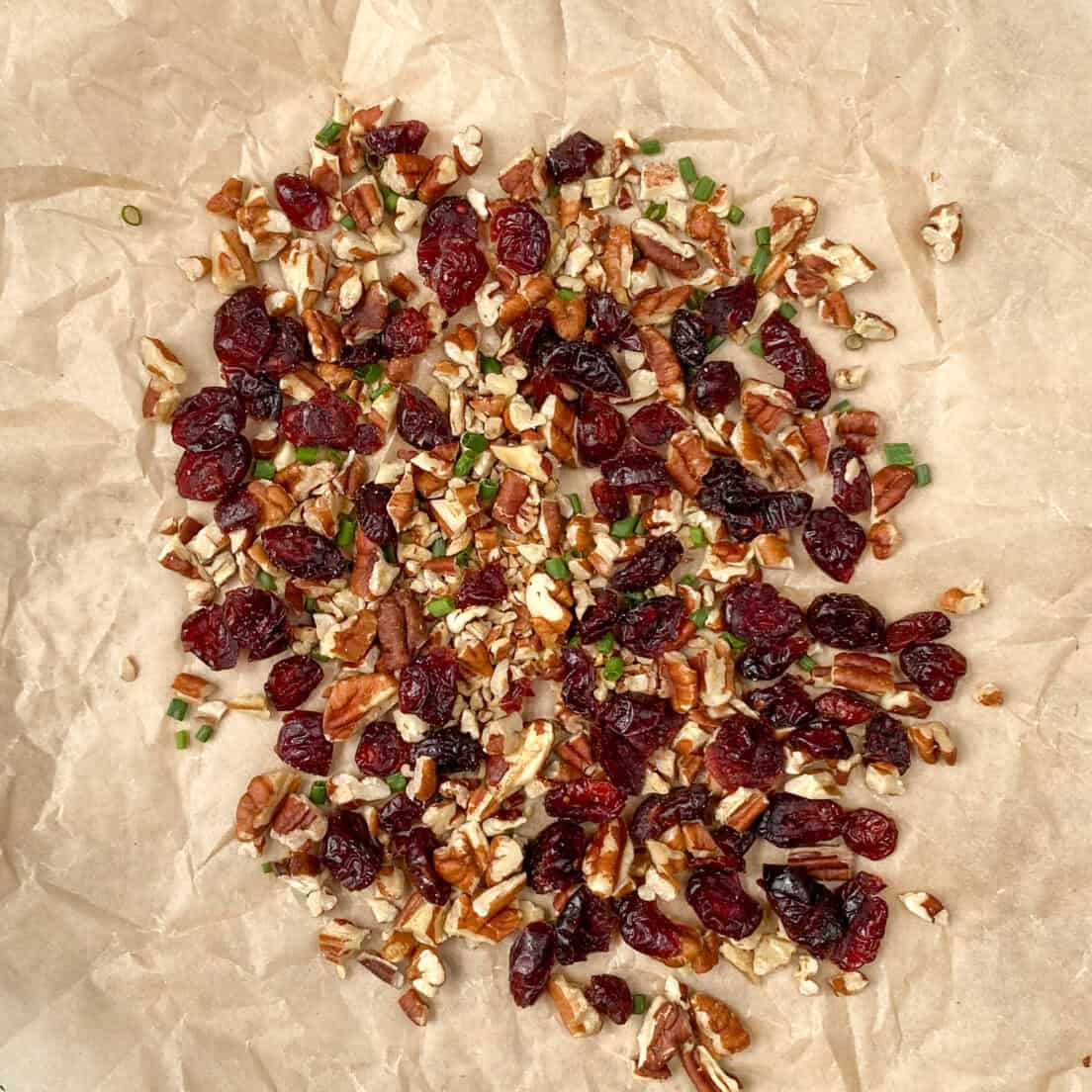 The pecan, cranberry and chives cheese ball coating all mixed together on a piece of crinkled brown parchment paper.