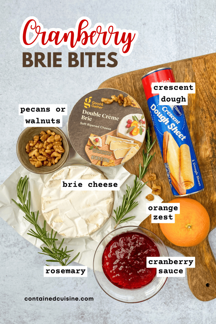 All the ingredients needed to make cranberry brie bites with labels, including a tube of crescent dough, wheel of brie cheese, small bowl with walnuts, bowl of cranberry sauce, an orange for zest and rosemary sprigs.