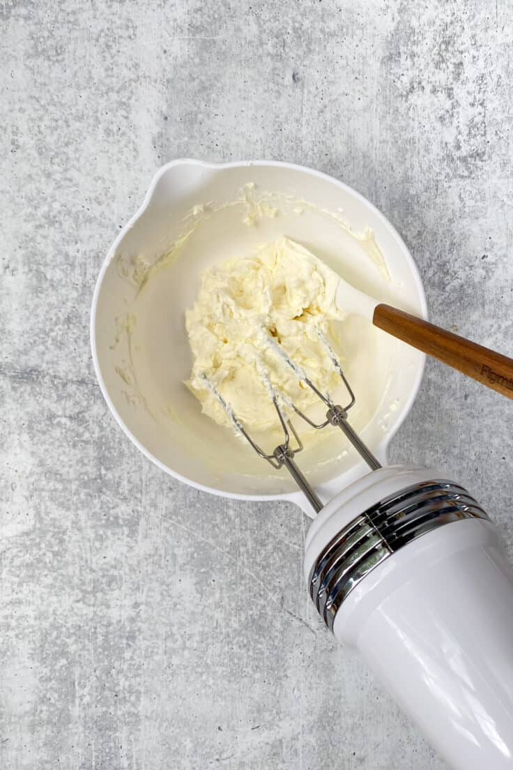 Beating cream cheese in a mixing bowl with an electric mixer.