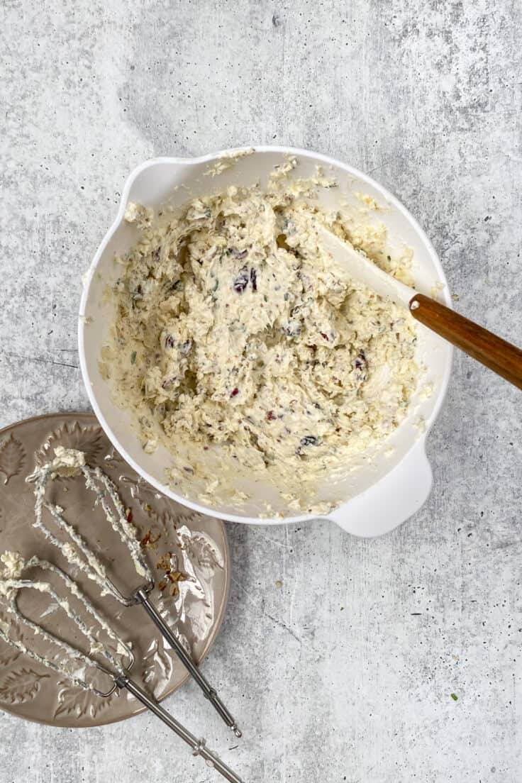 All the cheese ball ingredients beat together in a mixing bowl next to a small plate holding the two dirty beaters from the electric mixer.