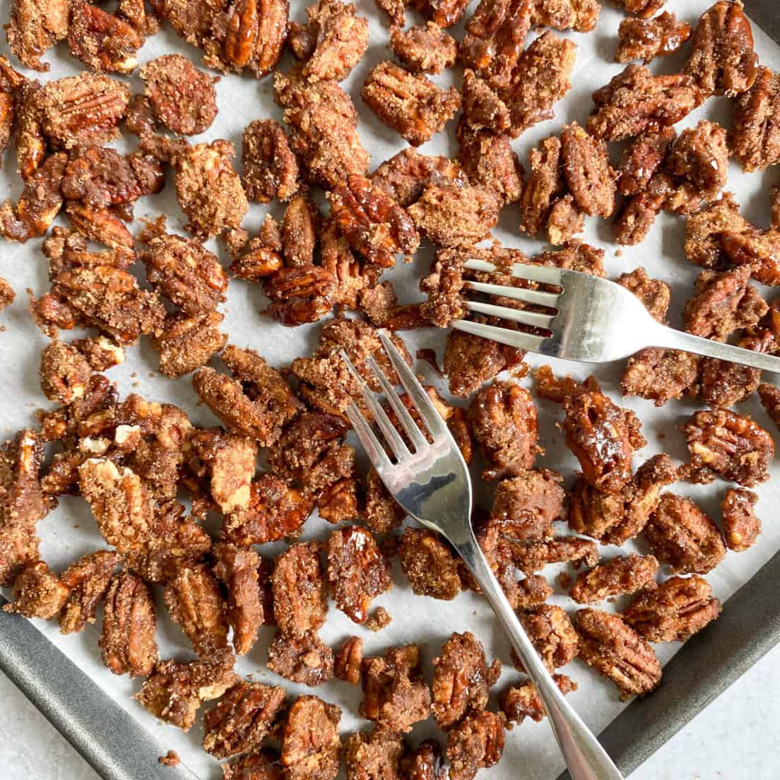 Candied pecans dumped on a baking tray and being pulled apart into a single layer with two forks.