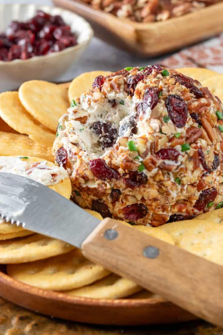 Pecan cheese ball with cranberries and chives that's been cut into with a small appetizer cheese knife and spread onto a cracker.