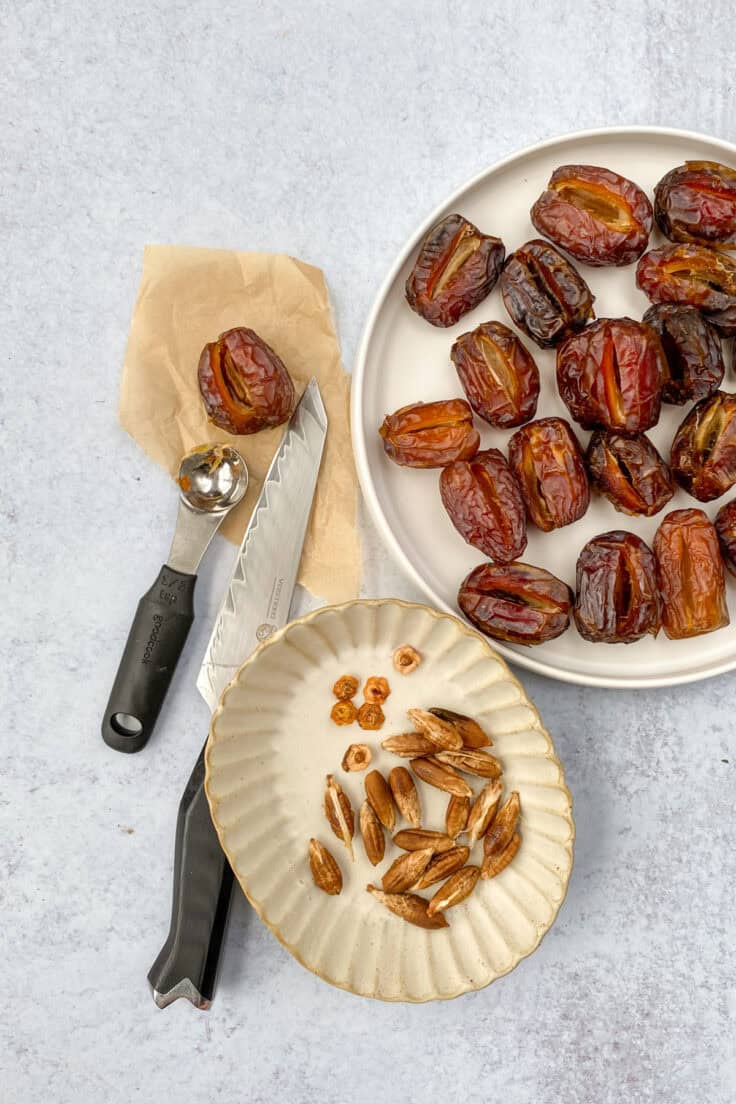 A plate of dates that have been pitted next to a knife and small bowl with the pits and dried stems in it.