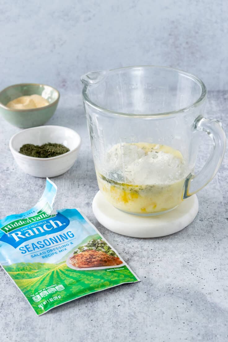 Ranch seasoning, dried dill and garlic powder added to melted butter in a glass measuring cup.