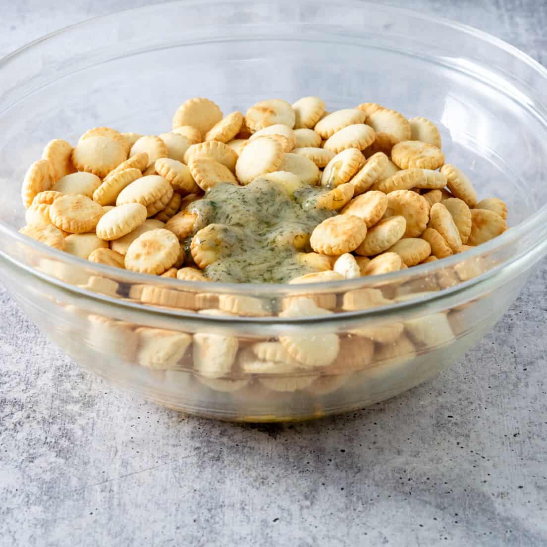 Plain oyster crackers in a large bowl with ranch butter mixture poured on top.