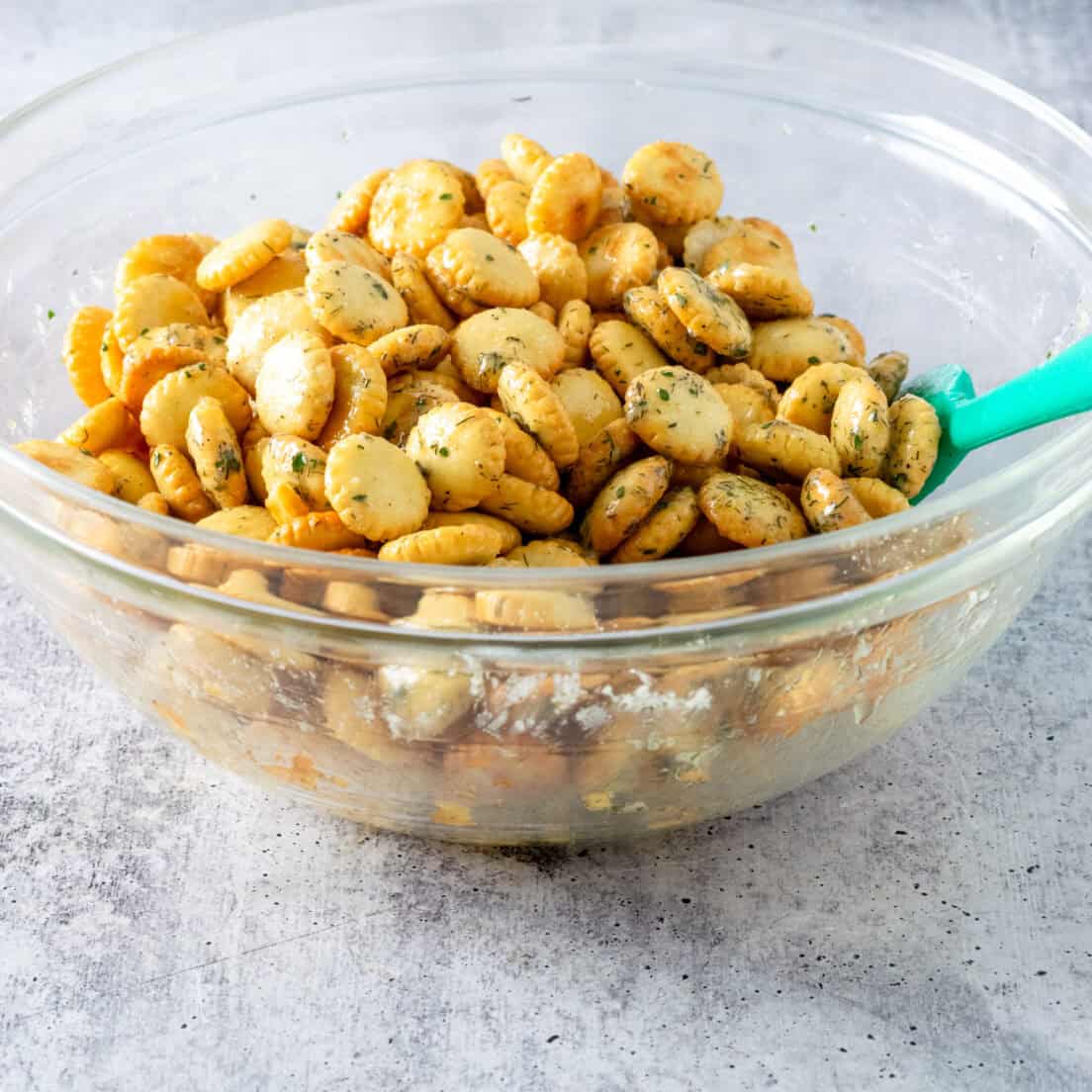 Stirring the oyster crackers and ranch  seasoned butter together with a green rubber spatula.