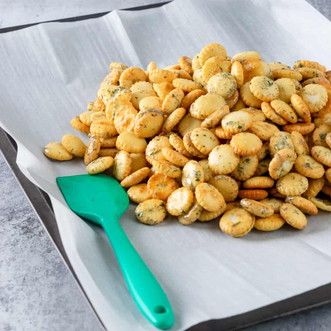 Coated crackers dumped on a parchment paper-lined baking tray.