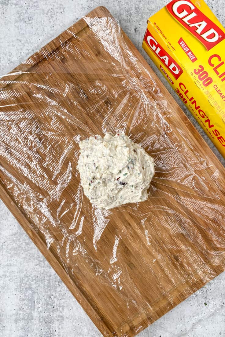 Inside of cheese ball on a sheet of plastic wrap which is sitting on top of a wooden cutting board and next to a package of cling wrap.