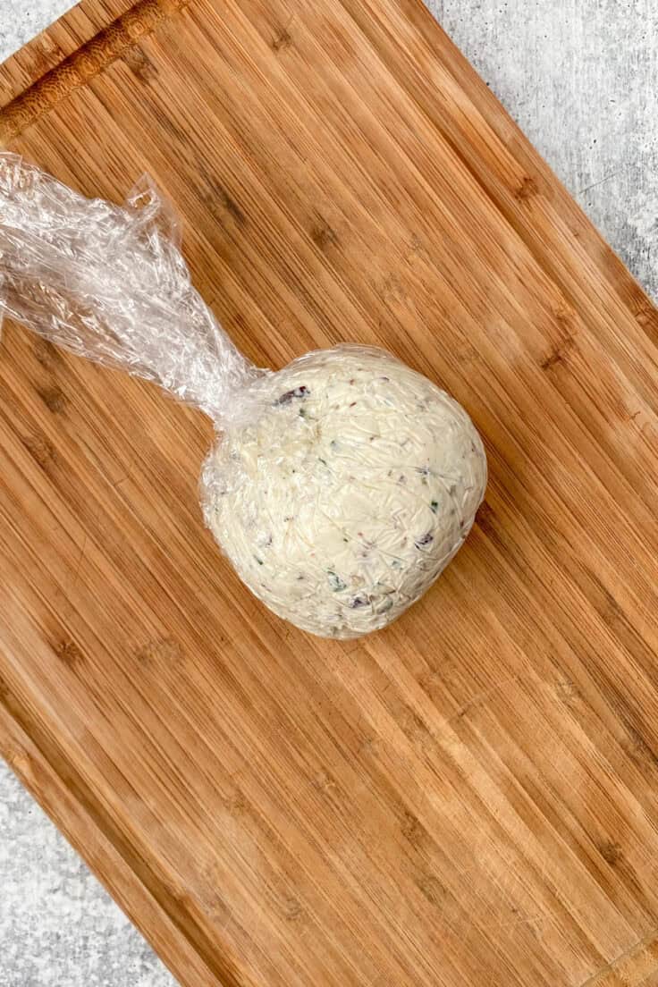 Inside of cheese ball covered in plastic wrap that's been shaped into a perfect ball with a flat bottom.