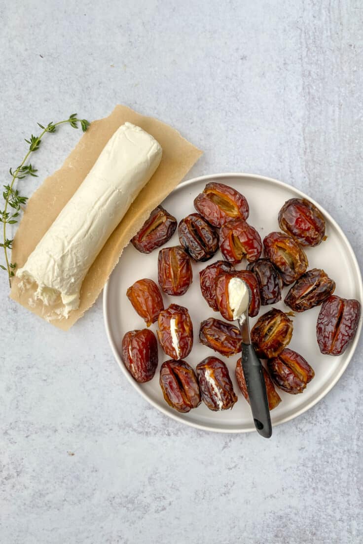 A log of goat cheese and sprig of thyme next to a plate of dates that with some stuffed with goat cheese.