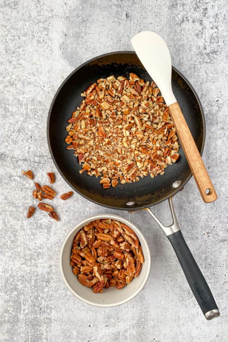 Chopped pecans being toasted in a pan on the stove.