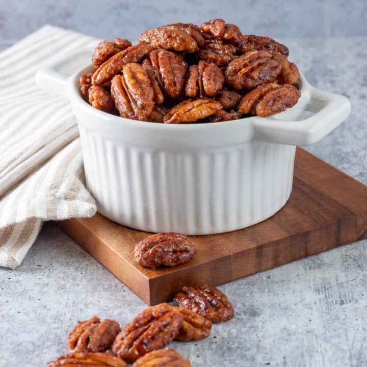 Small white bowl overflowing with homemade maple glazed pecans.