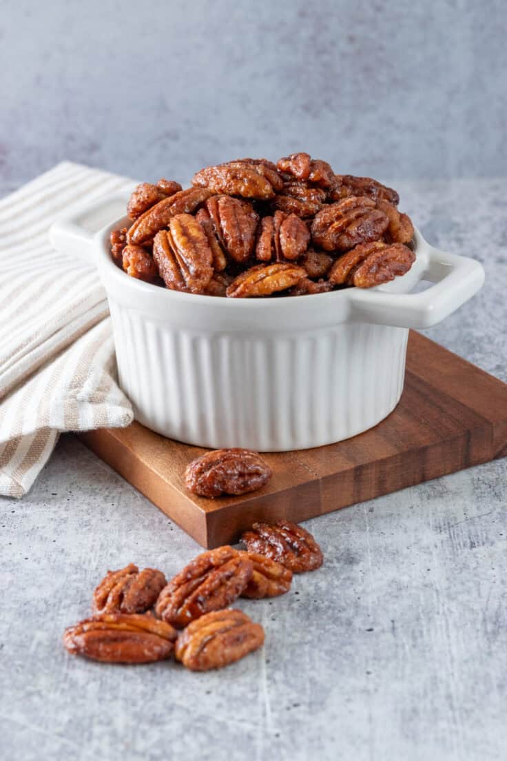 Small white bowl overflowing with homemade maple glazed pecans.