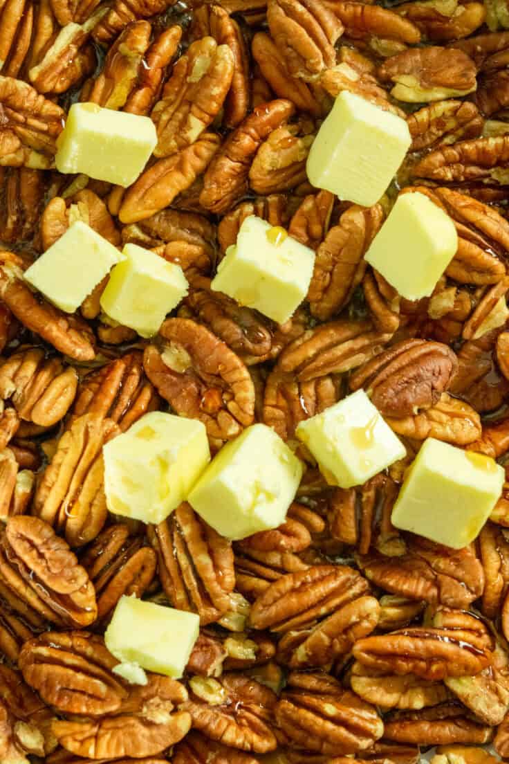 Raw pecans in a pan with chunks of butter and maple syrup poured all over.