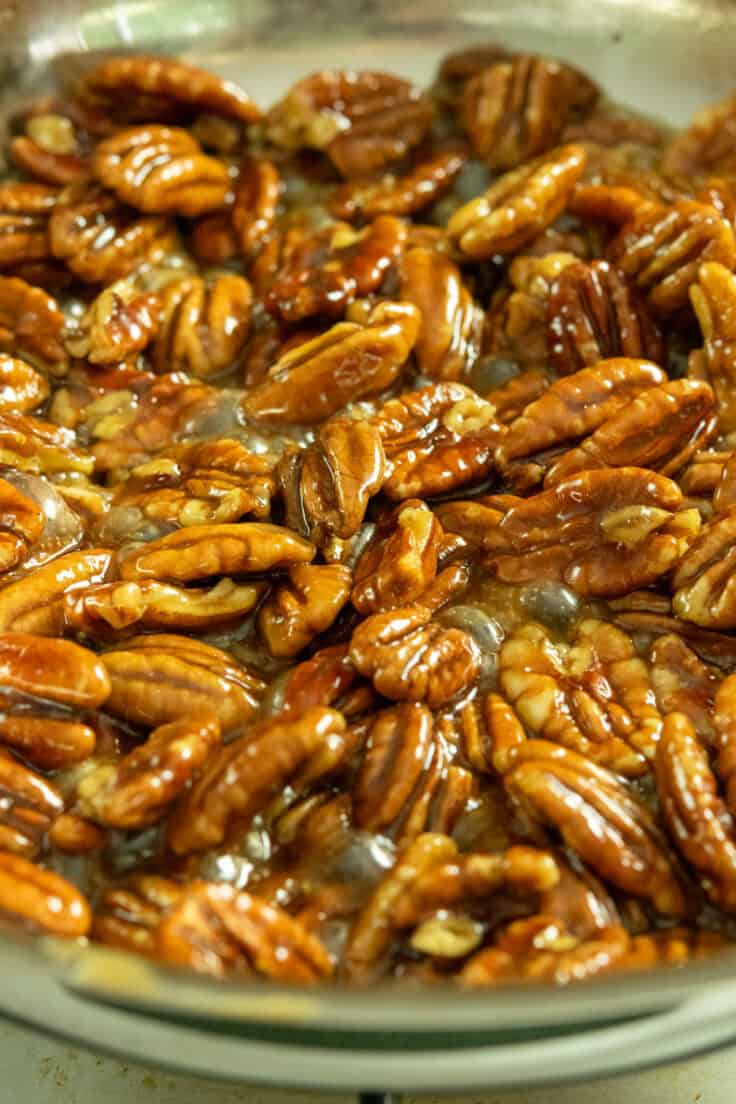 Maple candied pecans cooking on the stovetop showing how the glaze is reduced and sticking to pecans.