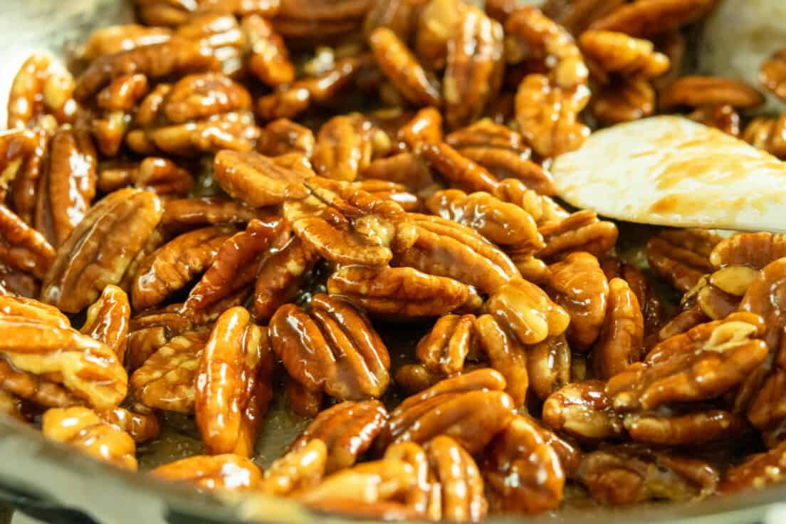 Pecans in a pan on the stove covered in a caramelized maple syrup glaze, ready to be removed from the heat.