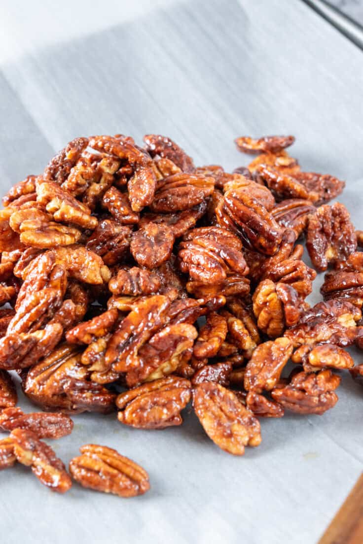 Maple pecans in a pile on a parchment paper lined baking tray.