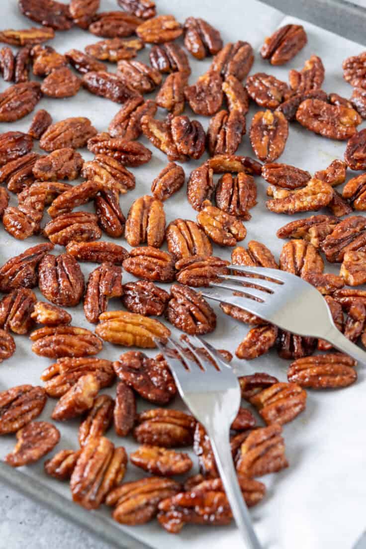 Two forks separating maple pecans on a tray into a single layer to cool.