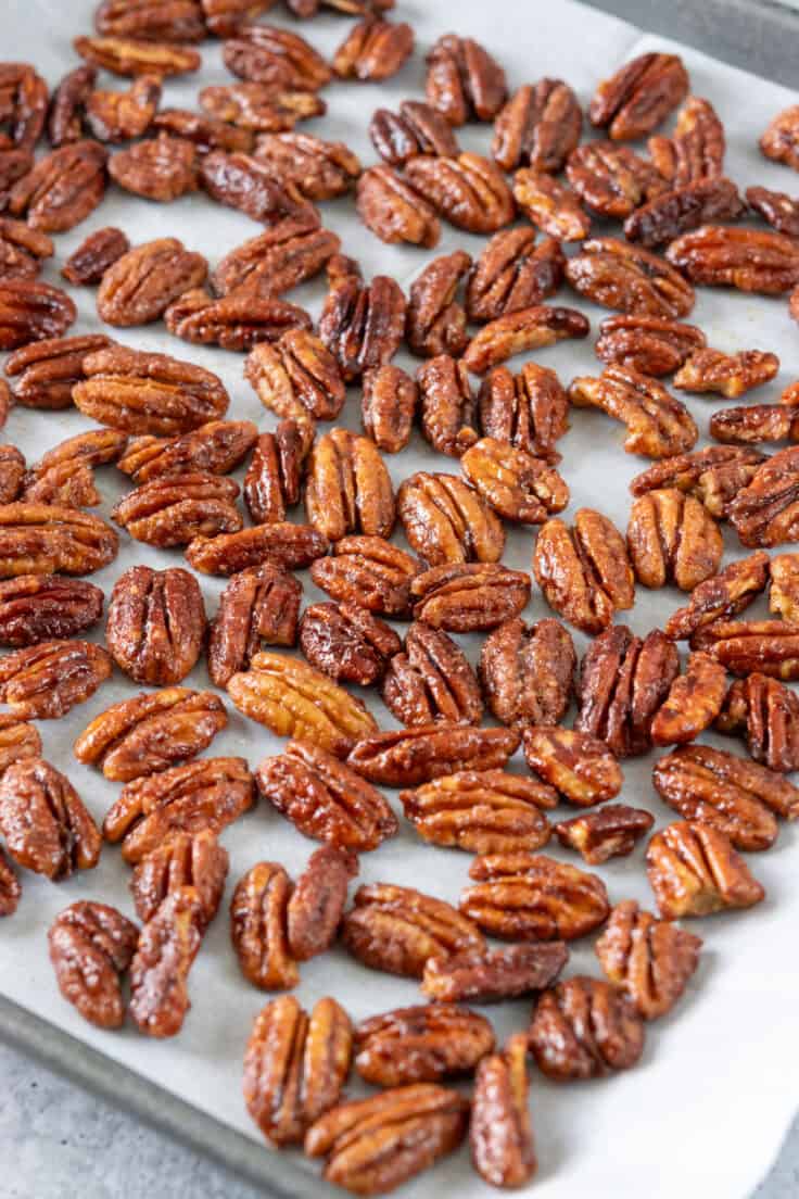 Maple candied pecans cooling in a single layer on parchment paper.